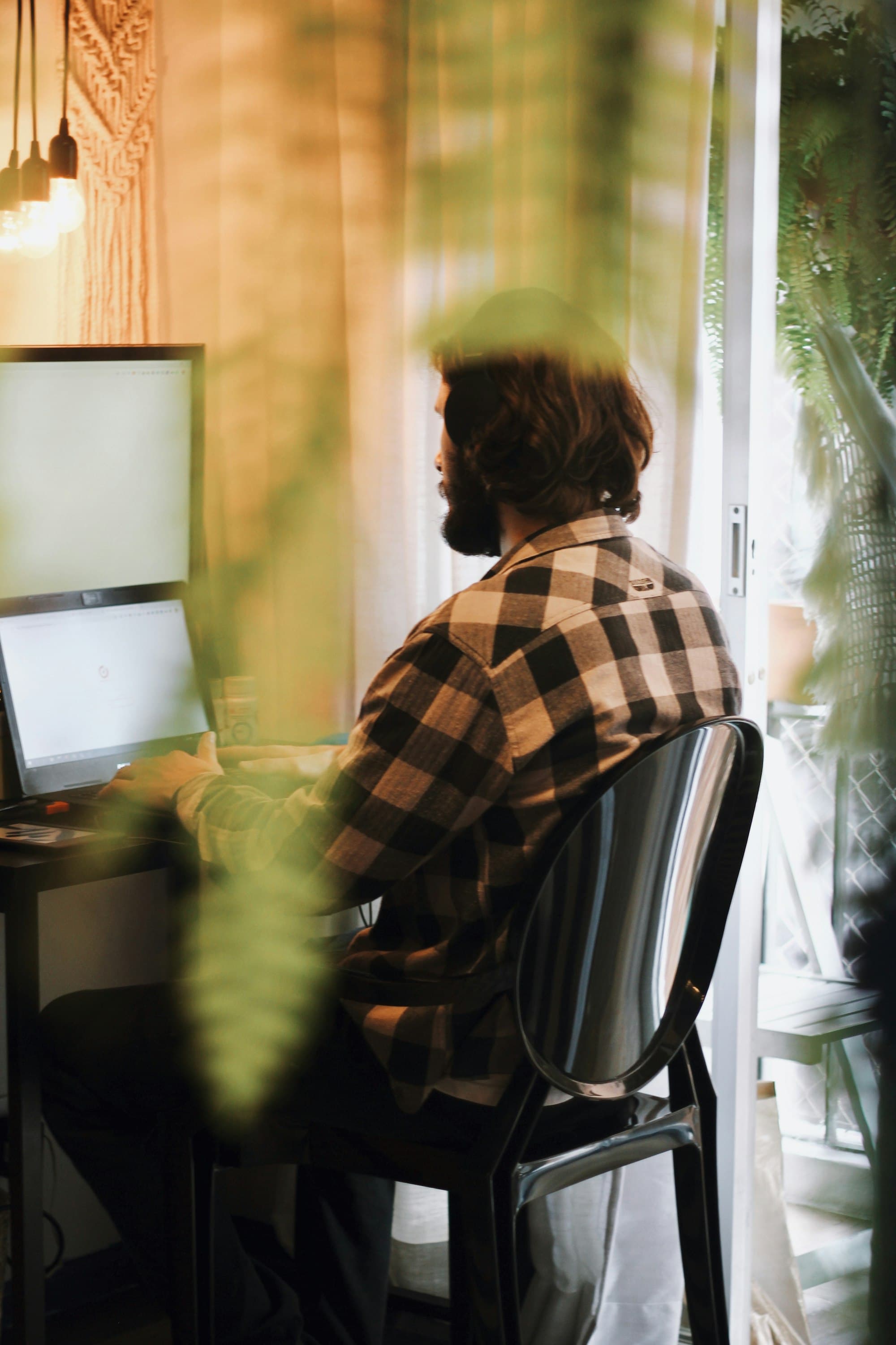 Someone working at a desk by a sunny window, framed by plants